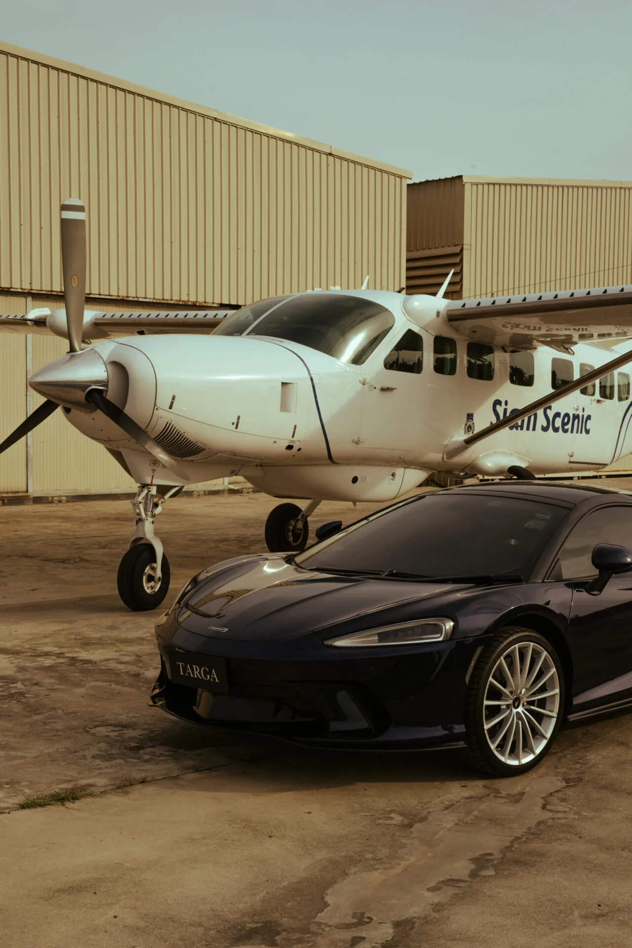 Dark blue luxury supercar parked in front of a private turboprop airplane