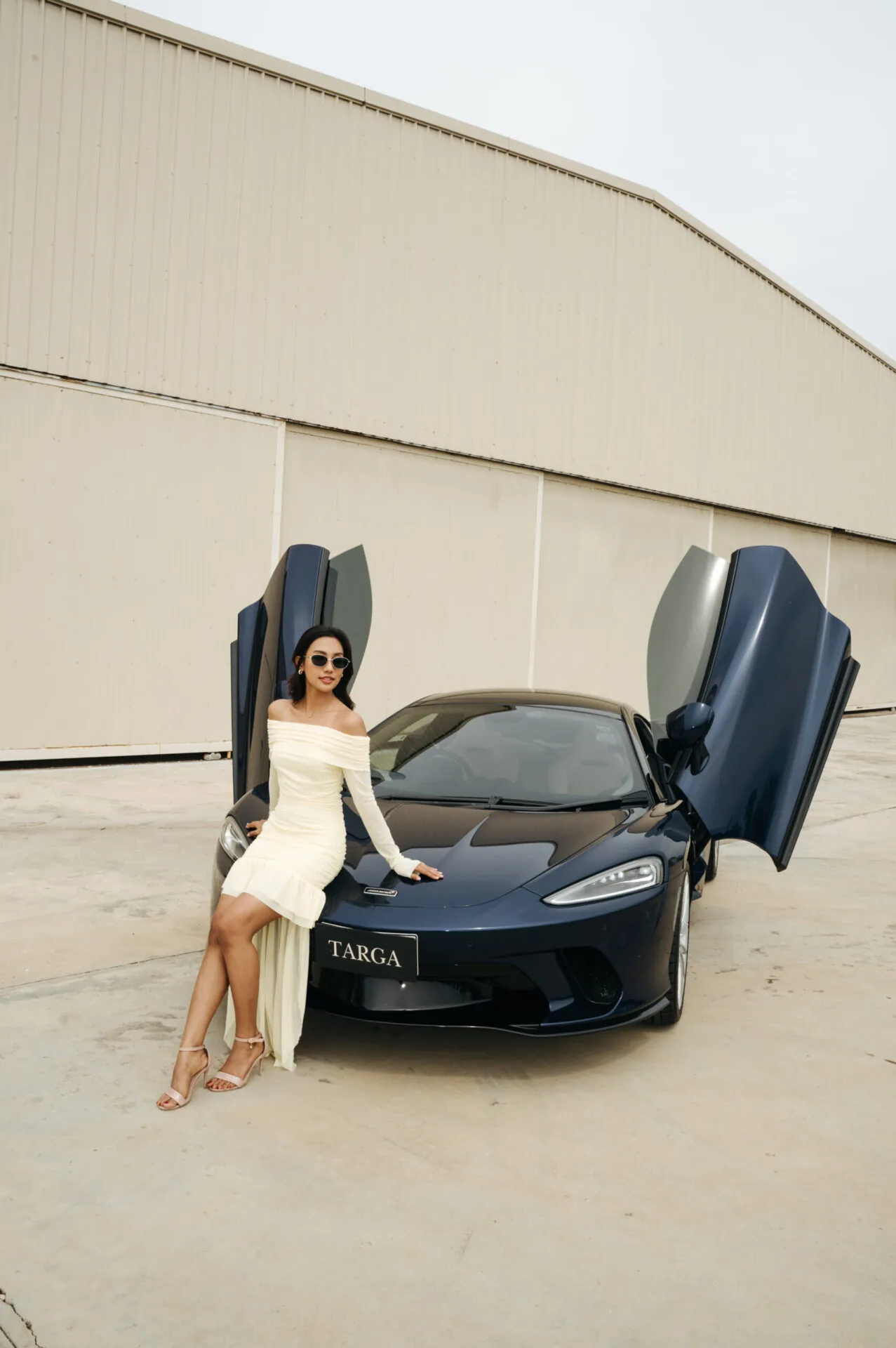 Woman sitting on the front bumper of a dark supercar with butterfly doors open