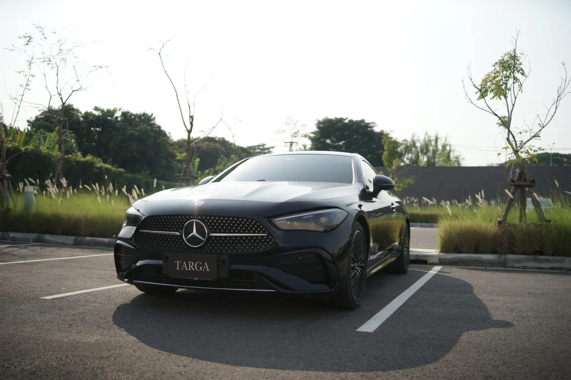 Man leaning against a luxury dark sedan supercar with a private plane in the background